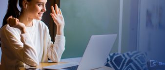 young lady raising her palm in front of her laptop, smiling